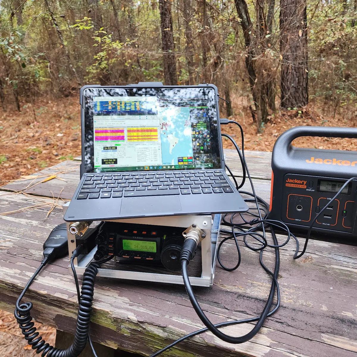 Portable field station on a picnic table in the woods — laptop, HF radio and a portable power station